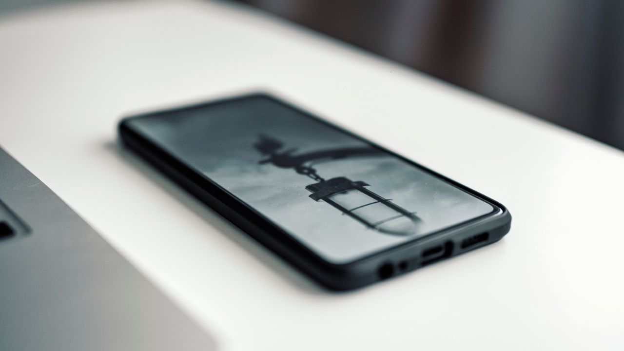Vue rapprochée d’un smartphone affichant une image floue, posé sur un bureau à côté d’un ordinateur portable.
